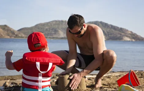 Child wearing a life jacket building in sand with dad