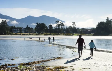 A parent and child walk on a sand spit on the beach at Tofino, British Columbia, a Pacific Northwest road trip destination for families