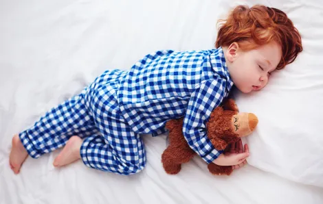 Young child with red hair sleeping and holding a stuffed animal