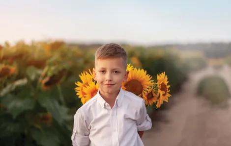 Little boy standing in front of a sunflower in a field