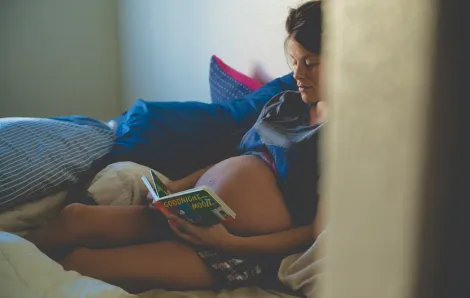 Pregnant woman sitting in a bed reading "Goodnight Moon"