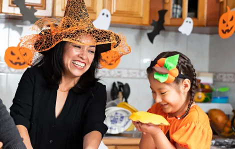 A happy mom and daughter wearing costumes in their kitchen prepare Halloween snacks and have fun together