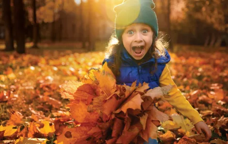 Young girl with a big smile holding a bunch of fall leaves