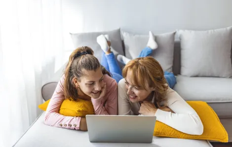 A mom and daughter lay on the couch on their bellies and look at a laptop; they're playing a mental health conversation starter game
