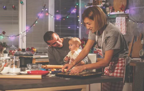 Family in a kitchen, mom making cookies and dad holding up baby who is sitting on the counter