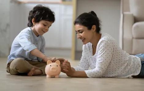Happy Indian kid his mom putting coins into a piggy bank