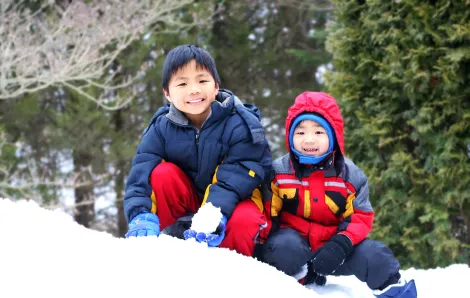 Two cute boys in jackets and hats play in the snow with trees forest in the background