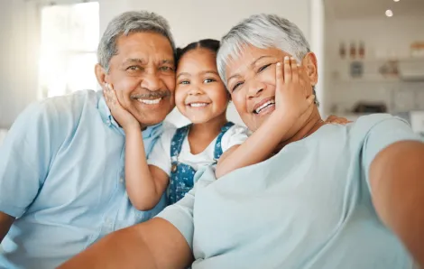Child sitting between grandparents with her hands on their faces, all smiling