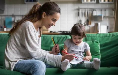 Teen girl sitting on a green couch with toddler girl coloring 