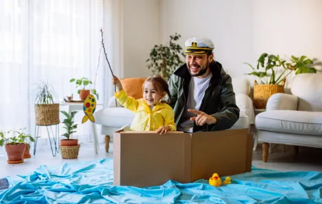 Dad and daughter sitting in a cardboard boat in a living room pretending to fish