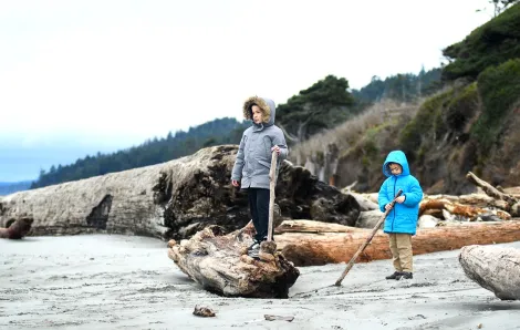 Boys in warm winter jackets standing on driftwood on a Pacific ocean beach on an off-season getaway to the Olympic peninsula