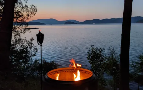 A fire in a fire pit near the water with mountains in the background