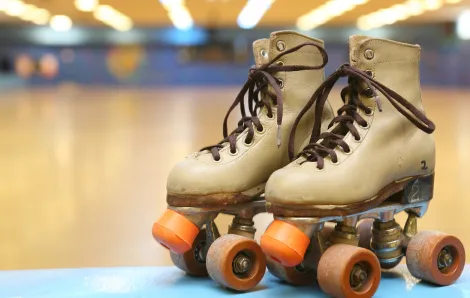 Close up view of a pair of roller skates, the rink's wood floor and lights are visible behind