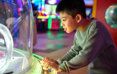 A tween-age boy about 11 plays an arcade game on a independence-building outing with friends around Seattle