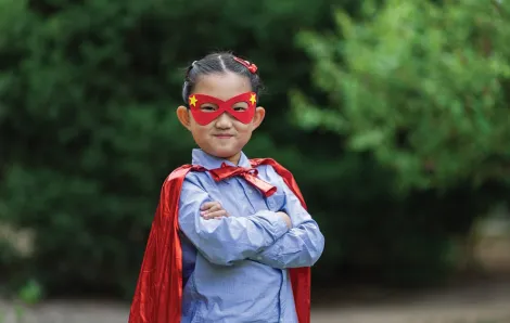 Little girl wearing a superhero costume smiling with her arms crossed