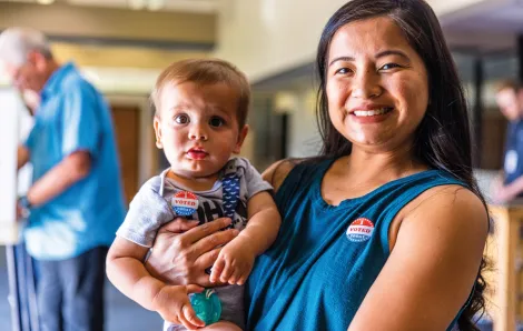 Mom holding a baby and are both wearing "I voted" stickers