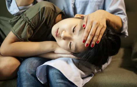 Young girl laying head in a parent's lap, feeling sick