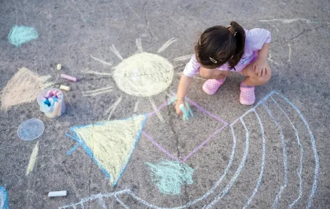 Young girl drawing with sidewalk chalk outside