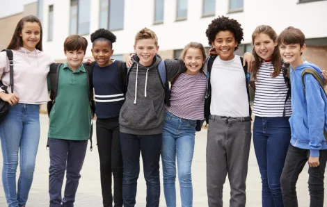 Group of tween kids standing in a line with their arms around each other smiling
