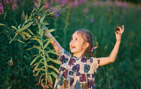 Young girl holding flowers in one hand and a pine cone in the other, looking happy in the sunshine 