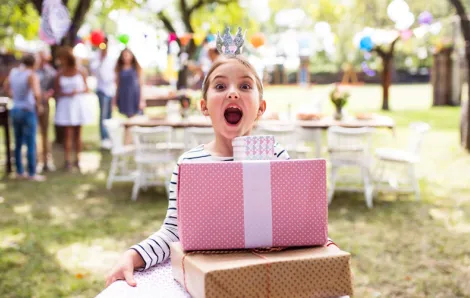 Young girl holding a stack of packages at a birthday party in a park, an easy outdoor birthday party idea for kids