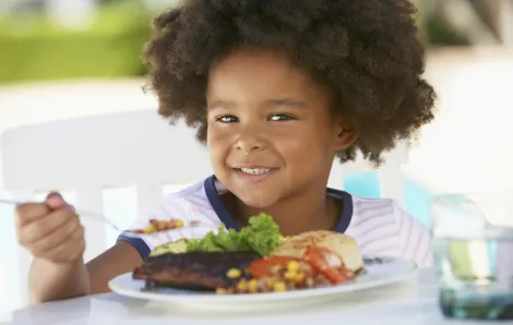 Young kid eating a plate of food at a BBQ