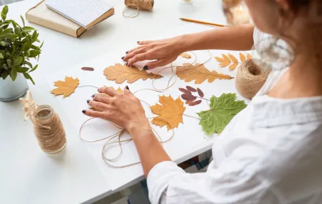 a woman strings leaves together for a fall craft for adults to make at a DIY party