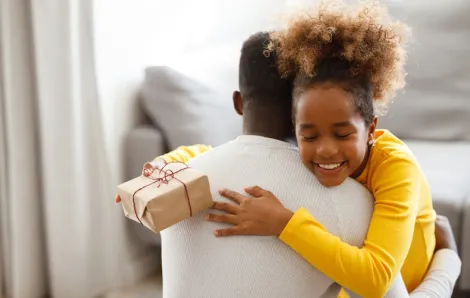 Girl hugging her dad and holding a gift 