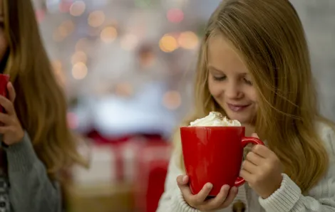 two young girls drinking hot chocolate from a big red mug 