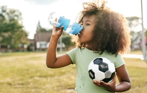 Young girl holding a soccer ball and drinking water at a sports camp in Seattle
