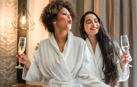 Two female friends relaxing in white robes holding champagne, credit iStock