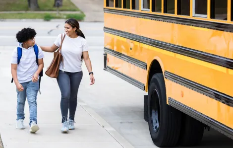 mom and son walking home after school next to a yellow school bus