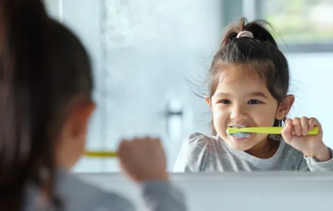 a little girl brushes her teeth in the mirror using tricks that helped her build a new habit