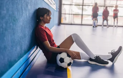 girl sitting down in a gym with soccer ball