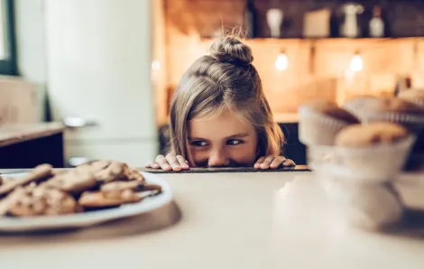 A girl spies a cookie on the counter, contemplating stealing it
