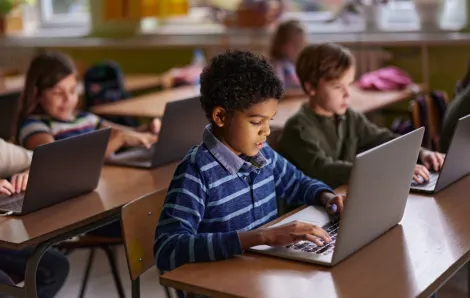 Kids sitting in a classroom all looking at laptops