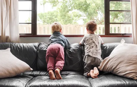 two kids sitting on a couch looking outside