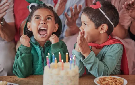 An excited child wearing a costume sits in front of cake at a toddler birthday
