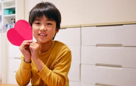 A boy holds a red heart while making crafts for Valentine's Day.