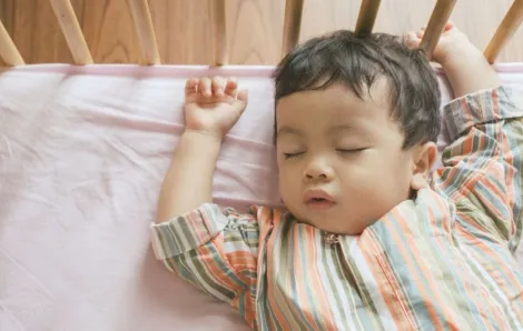 Little boy toddler adorably sleeping in his baby cot