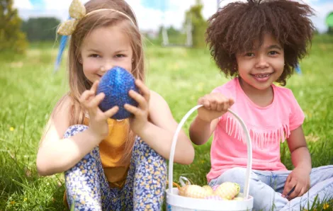 Two girls sitting on grass, holding eggs and basket for Easter.