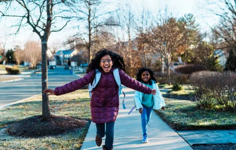 two girls running down the street happy to be out of school
