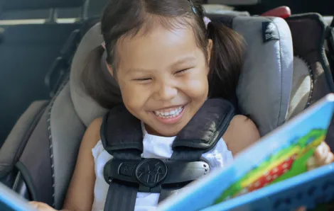 girl in a car seat with a fun car toy happy on a road trip