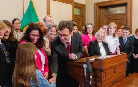 Gov. Bob Ferguson handing over his pen to a child