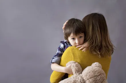 Sad boy holding mom tight with teddy bear