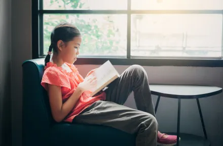 Cute little Asian girl reading a book in the living room at home