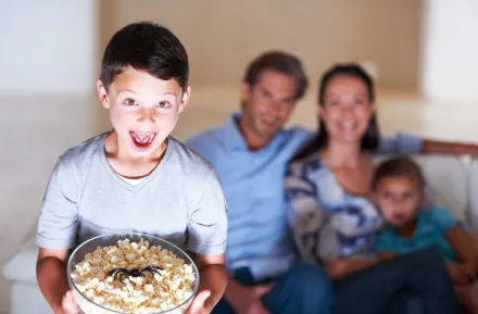 boy holding a bowl of popcorn with a plastic spider in it with his family on the couch in the background