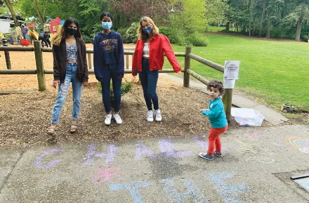 Adults and a child at a park drawing with sidewalk chalk