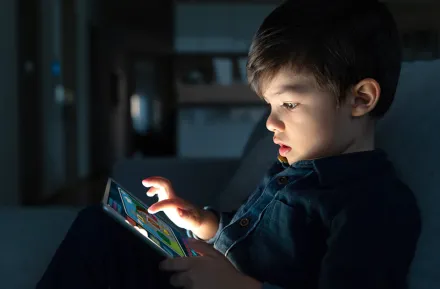 Boy sitting on the couch playing games on a tablet.