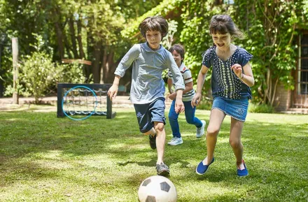 Three kids playing soccer in the backyard